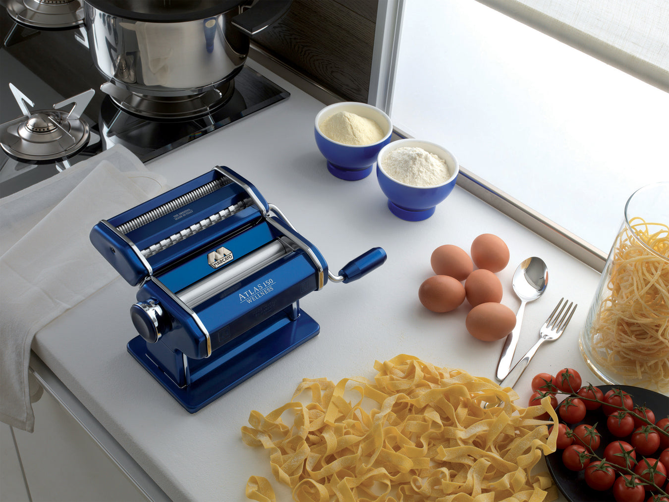 Marcato Italian Pasta Maker Blue on a kitchen counter top with freshly rolled pasta and eggs
