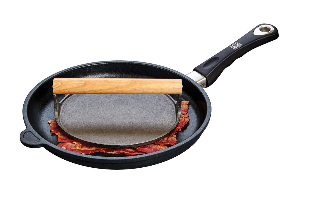 round cast iron bacon press with pig design face down in frying pan on top of bacon